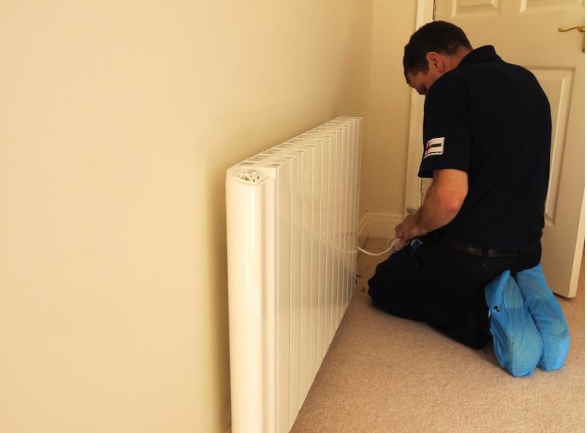 A man works on a baseboard water heating system in a home.